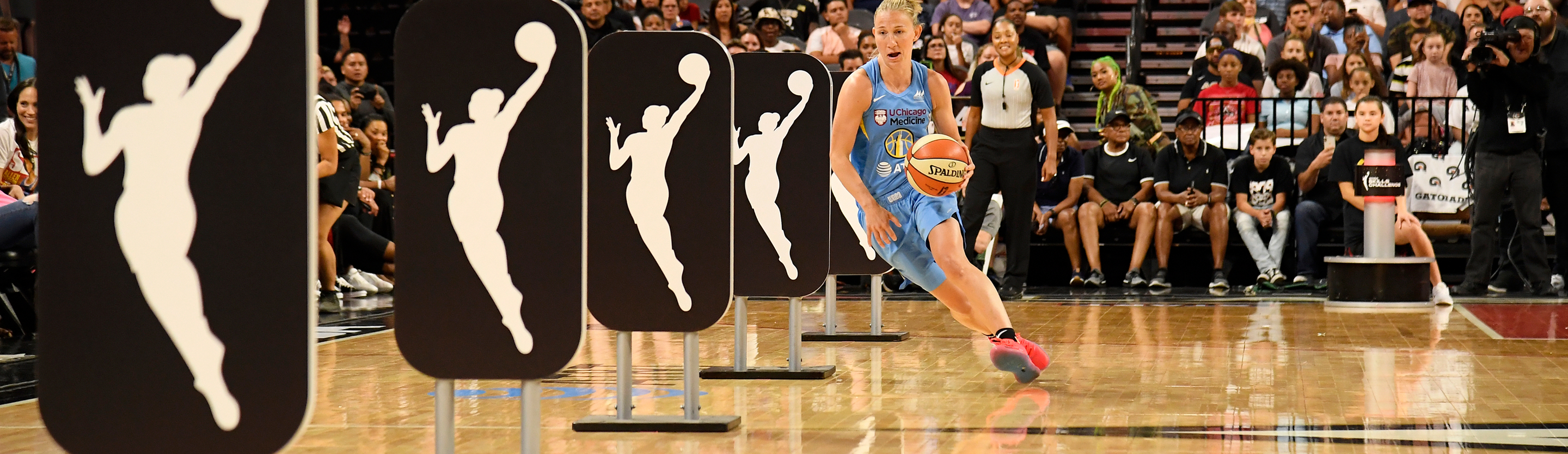 WNBA player in a light blue Chicago Sky uniform dribbles through WNBA logo obstacle panels during a skills challenge