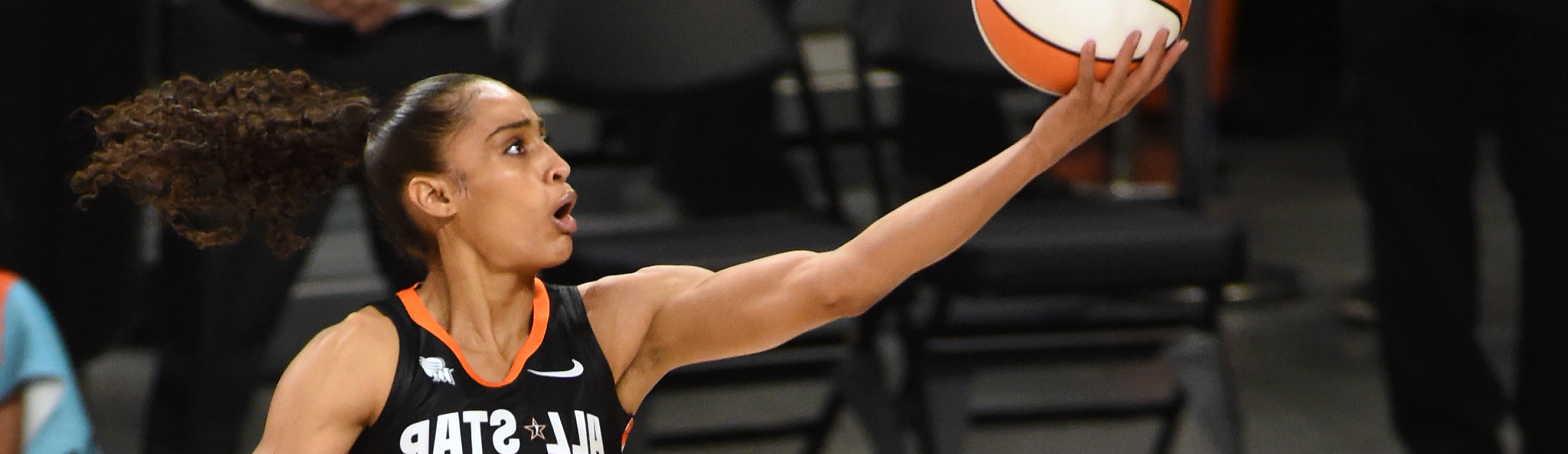 WNBA All-Star player in black uniform extends to lay the ball up near the basket